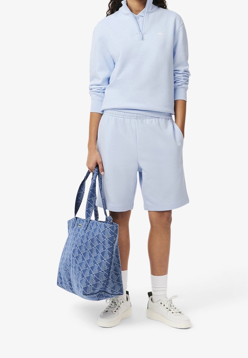 Felpa azzurra con zip, pantaloni corti abbinati, sneakers bianche e una borsa a tracolla blu con motivo, dotata di doppio manico. Materiale in misto cotone.