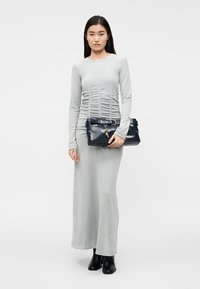 Siva obleka z dolgimi rokavi z nabrano teksturo, kombinirana s temno modro usnjeno torbico z okrasnimi detajli in naramnico. Črni gležnjarji.