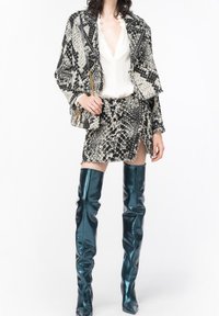 Svartvit slagormmönstrad kavaj med fransar, parat med en figursydd kjol och glansiga turkosa överknästövlar. Inkluderar en liten väska.