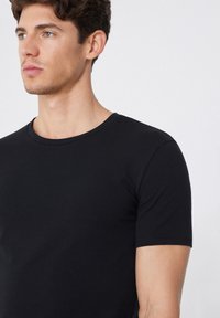 Černé tričko s krátkým rukávem, kulatým výstřihem, hladký bavlněný materiál, přiléhavý střih, minimalistický styl, bez viditelných vzorů nebo akcentů.