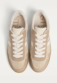 Scarpe sportive beige con tomaia in mesh testurizzato, dettagli in pelle bianca e lacci piatti. La suola in gomma offre aderenza e stabilità.