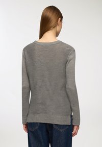 Szary dzianinowy sweter z długimi rękawami, okrągłym dekoltem i bocznymi rozcięciami na dole. Gładka tekstura, swobodny krój, w połączeniu z ciemnoniebieskimi dżinsami.