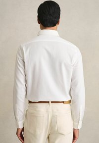 Cămașă albă cu mâneci lungi și manșete cu nasturi, asortată cu pantaloni bej deschis, ambele având o textură netedă și un design croit.