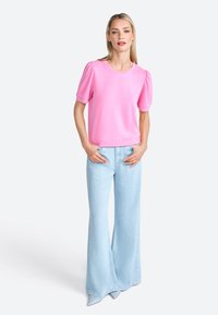 Top rosa a maniche corte con maniche a sbuffo, abbinato a jeans a zampa di elefante blu chiaro. Il materiale sembra morbido; texture liscia; design semplice.
