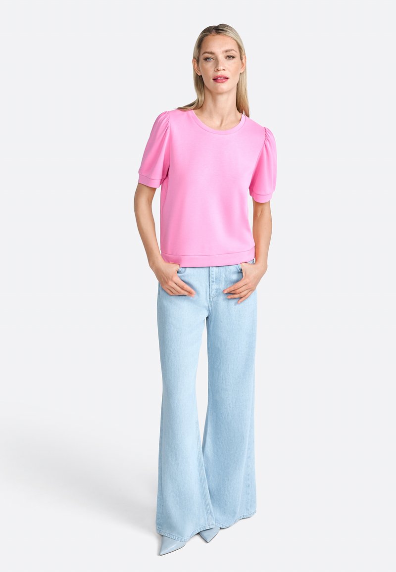 Top rosa a maniche corte con maniche a sbuffo, abbinato a jeans a zampa di elefante blu chiaro. Il materiale sembra morbido; texture liscia; design semplice.