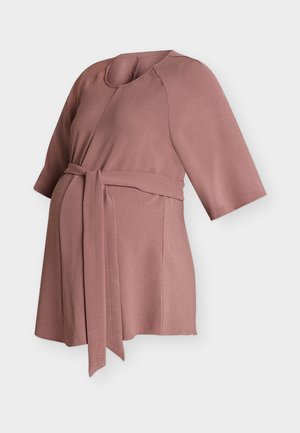 Haut de maternité mauve avec des manches mi-longues jusqu'au coude et une ceinture à nouer à la taille, conçu pour le confort et le style pendant la grossesse.