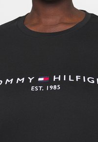 Zwart katoenen T-shirt met witte geborduurde tekst "TOMMY HILFIGER" en detail "EST. 1985", met een rood en blauw accentlogo.