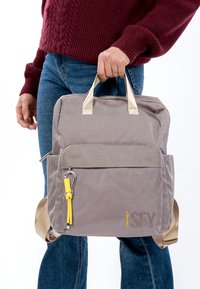 Szary plecak w wzory z górnym uchwytem i regulowanymi paskami na ramiona. Posiada żółte akcenty i zewnętrzną kieszeń na zamek. Gładka faktura.