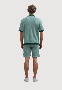 Short-sleeve polo shirt and shorts set in teal with a textured pattern, featuring dark green accents on collar and hems.