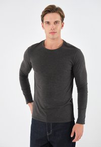 Donkergrijze lange mouwen shirt van een zacht materiaal met een ronde halslijn, aansluitend ontwerp en naadloze manchetten, gecombineerd met donkere spijkerbroek.