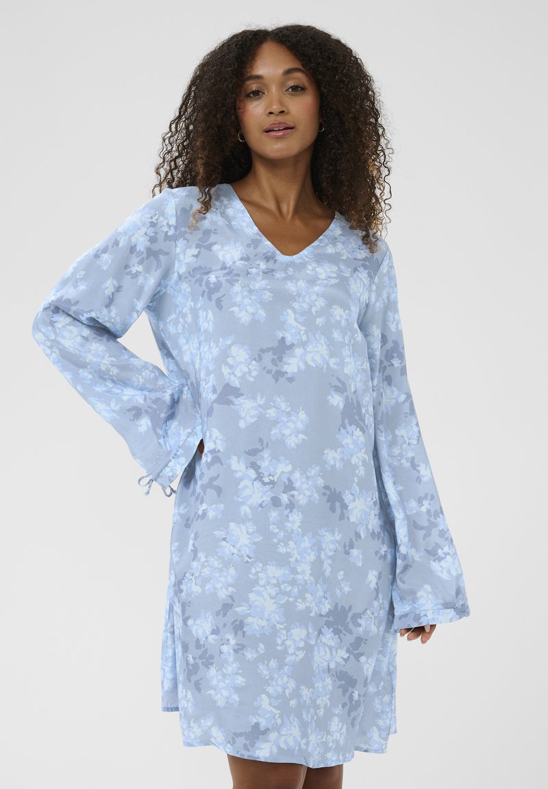 Hellblaues Blumenkleid mit langen Ärmeln, V-Ausschnitt und seitlichen Schlitzen. Der Stoff hat ein weiches, strukturiertes Muster mit dunkleren blauen Akzenten.