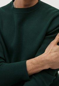 Dunkelgrüner strukturierter Pullover mit Rundhalsausschnitt, ausgestattet mit gerippten Bündchen und Saum. Der Stoff wirkt weich und eng am Körper anliegend.