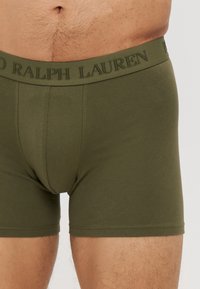 Boxerii scurți de culoare verde măslin, fabricați dintr-un material moale, cu un tiv elastic pe care se află logo-ul "RALPH LAUREN". Design strâns și textură netedă.