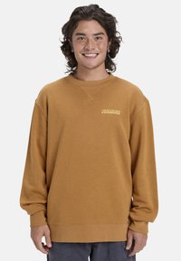 Felpa in pile marrone con colletto a girocollo, vestibilità comoda e logo Quiksilver in giallo chiaro sul petto. Texture morbida e maniche lunghe.