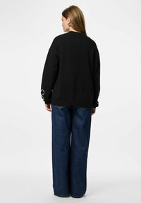 Pull en maille noir à coupe décontractée, avec des accents blancs cousus sur les manches. Associé à un pantalon en denim bleu foncé ample.