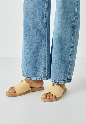 Des sandales slides couleur beige en matière lisse présentent un design à bout ouvert avec un détail découpé et une semelle claire. Portées avec un pantalon large en denim.