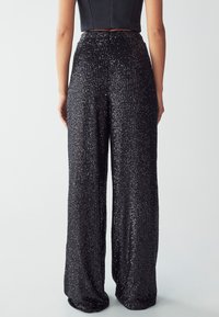 Pantaloni larghi neri in paillettes con vita alta, caratterizzati da una superficie testurizzata e decorazioni lucenti in tutto il tessuto.