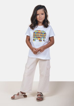 Camiseta blanca con un gráfico colorido de elefante, pantalones cargo crema con bolsillos, y sandalias grises con hebillas. Diseño simple y casual.