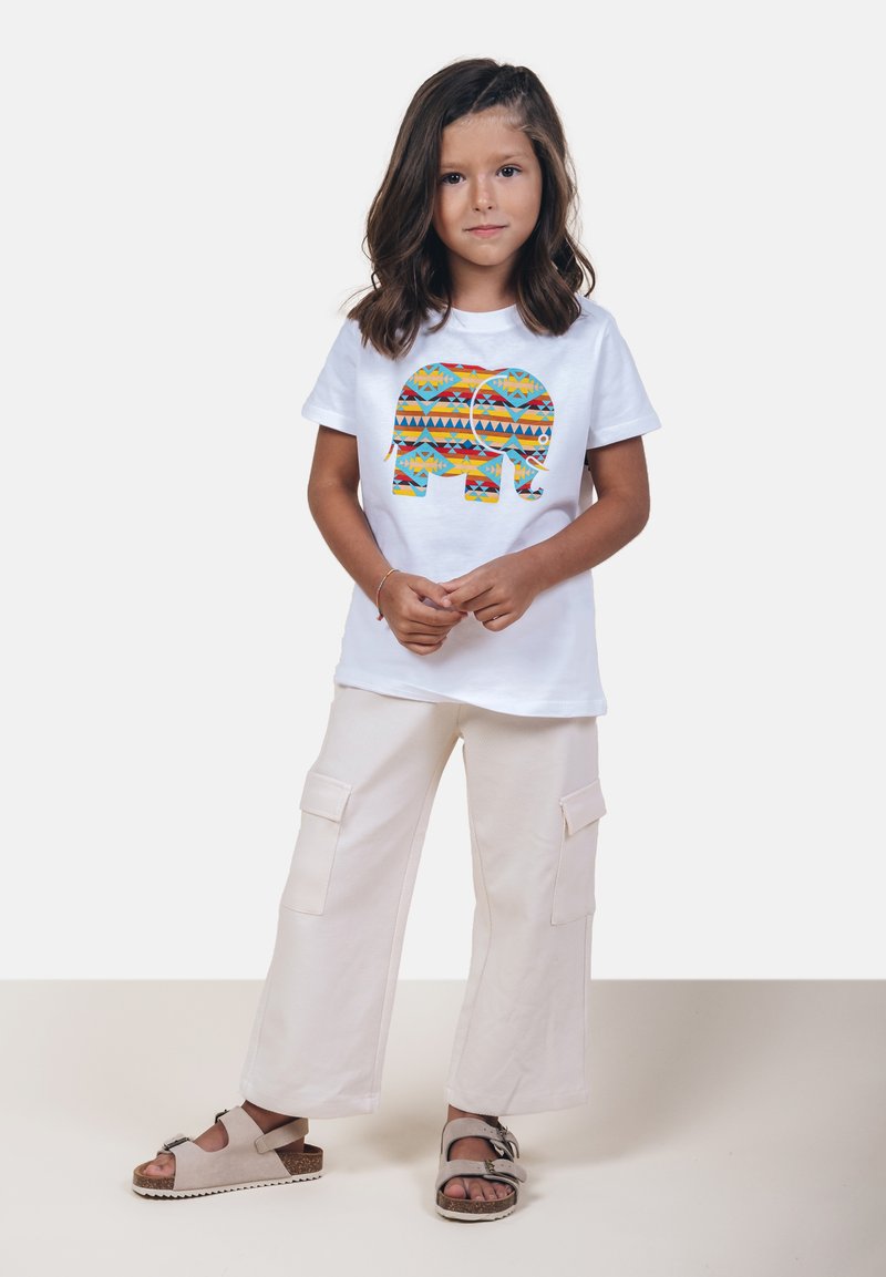 Camiseta blanca con un gráfico colorido de elefante, pantalones cargo crema con bolsillos, y sandalias grises con hebillas. Diseño simple y casual.