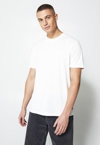 White cotton t-shirt with short sleeves, round neckline, and a relaxed fit, paired with dark gray jeans; smooth texture and simple design.