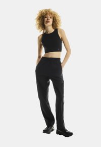 Black cropped tank top with a round neckline, paired with black, relaxed-fit pants featuring side pockets and a smooth texture. Black sneakers included.