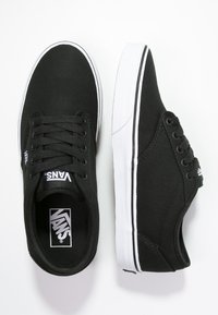 Sneaker nere in tela con design a basso profilo, suola in gomma bianca e righe bianche a contrasto. Presentano sei fori per i lacci e il logo Vans.