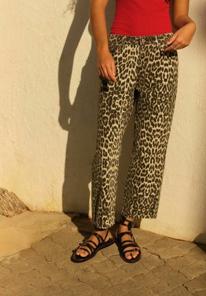 Luipaardprint tapered pants in beige en zwart, gecombineerd met zwarte sandaaltjes met bandjes. Getextureerde stof, vijf-pocket ontwerp, zichtbare stiksels.