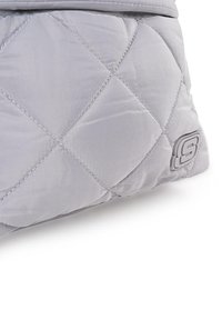 Bolsa de tela gris acolchada con un acabado suave, que presenta costuras diagonales, un acento de logo y una forma triangular en la base.