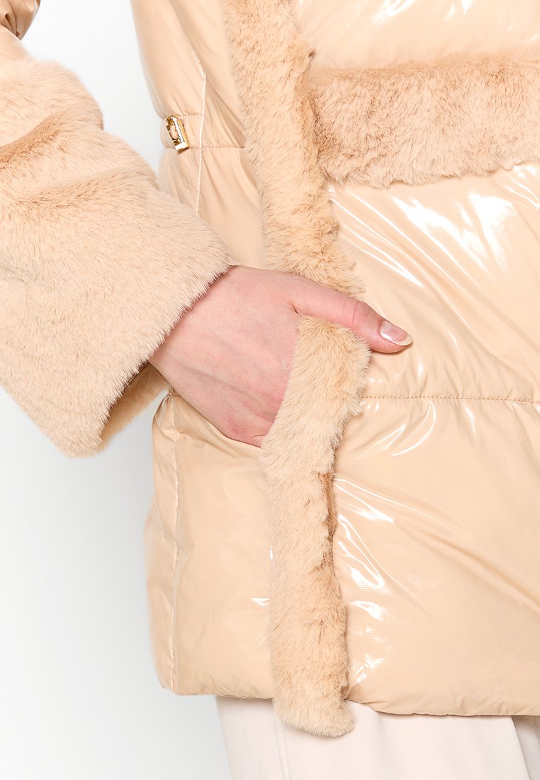 Beige gepolsterte Jacke mit glänzender, glänzender Außenfläche und weichen, Kunstfell-Akzenten entlang der Kanten und Taschen. Verfügt über einen Reißverschluss und Seitentaschen.