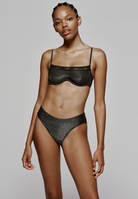 Zwarte bh en hoge bikiniset in een gestructureerde, metallic stof. De bh heeft smalle bandjes en een semi-doorzichtige rand aan de bovenkant.