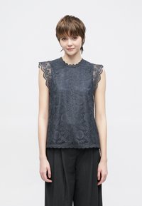 Tumši pelēks mežģīņu tops ar viļņotām malām, ziedu rakstiem un īsām piedurknēm. Kombinēts ar plaša piegriezuma tumšām biksēm.