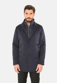 Cappotto blu navy dal design su misura, con colletto a revers, chiusura a bottoni e tasche laterali. Tessuto liscio con minime rifiniture.