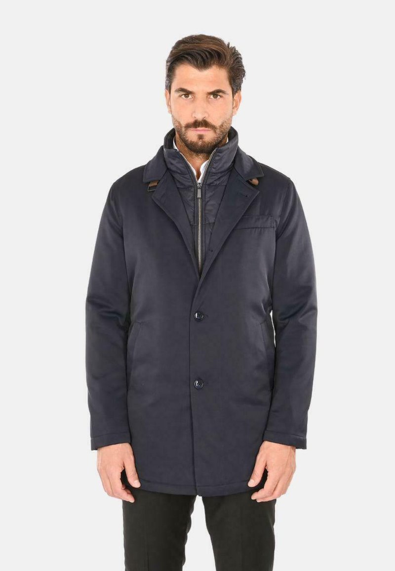 Cappotto blu navy dal design su misura, con colletto a revers, chiusura a bottoni e tasche laterali. Tessuto liscio con minime rifiniture.