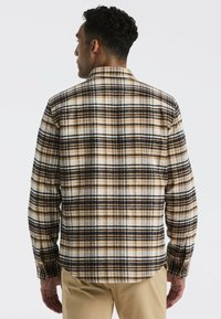 Heren geruit overhemd met een achteraanzicht in bruin, zwart en crème. Gemaakt van een zachte stof met een knoopsluiting bij de kraag en manchet.