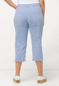 Pantalones de algodón azul claro, con un corte tapered y longitud a media pantorrilla, que cuentan con dos bolsillos traseros y puños. Combinados con zapatos blancos tipo slip-on.