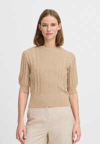 Pullover beige lavorato a maglia con motivi a treccia, maniche a palloncino corte e orlo a coste, abbinato a pantaloni di colore chiaro.