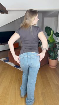 Jeans flare de um azul claro com uma cintura de altura média, quatro bolsos, detalhes de costura e uma bainha desfeita, combinados com uma t-shirt ajustada de cor cinza escuro.