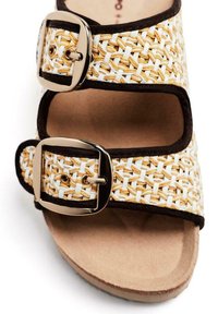 Sandalo intrecciato con un design beige e bianco, due fibbie regolabili dorate e un bordo marrone; superficie testurizzata con una suola imbottita.