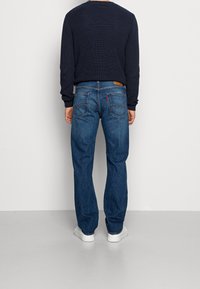 Marinblå tröja med strukturstickning, som kombineras med blå denimjeans med en läderlogotyp på bakfickorna och en röd tab. Vita sneakers.