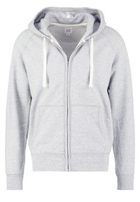 Sudadera con cremallera de color gris claro con cordones blancos, bolsillos frontales y una pequeña etiqueta visible de la marca GAP en el interior del cuello.