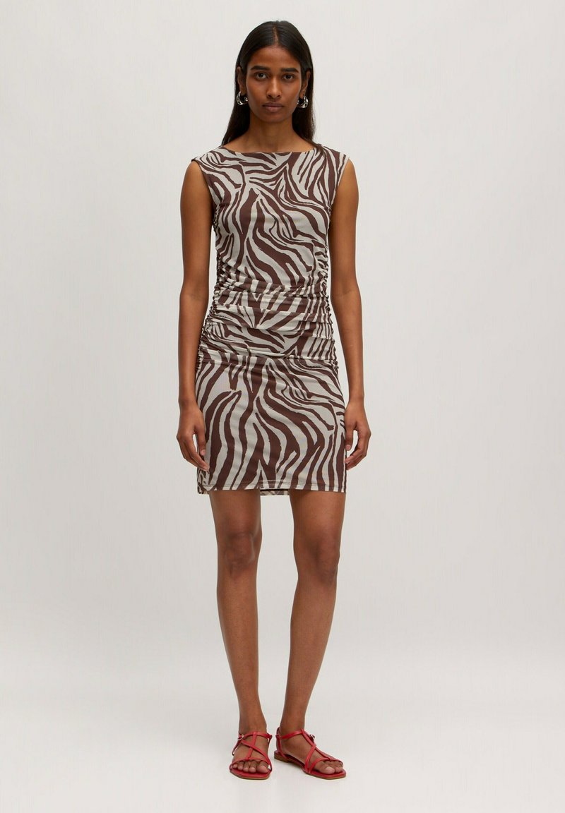 Braunes und cremefarbenes, gestreiftes Kleid im Zebra-Look mit taillierter Silhouette, kurzen Ärmeln und gerafften Seitendetails. Getragen mit roten flachen Sandalen.