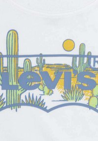 Camiseta blanca de algodón con un diseño colorido de cactus y paisaje desértico, con el texto azul "Levi's" y un sol amarillo.