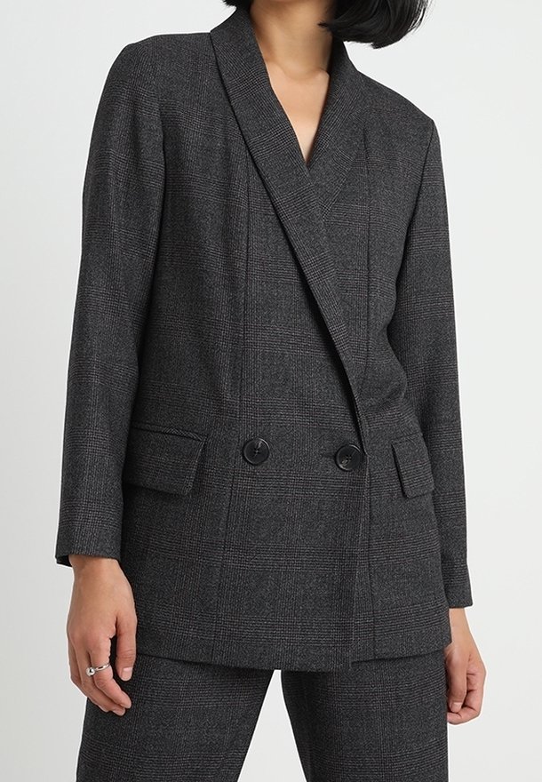Šedý kostkovaný dvouřadý blazer s klopovým límcem, dvěma předními kapsami a černými knoflíky. Hladká textura a přizpůsobený design.