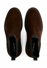 Stivaletti alla caviglia in suede marrone con pannelli elastici neri sui lati, punta tonda e suola in gomma tessurizzata. Presentano un linguetta sul retro per facilitare l'indossamento.