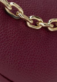 Borsa in pelle borgogna con superficie testurizzata, completata da una tracolla in chain gold lucido con anelli ovali e finitura liscia.