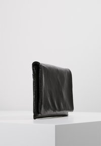 Pochette en cuir noir au texture lisse et brillante. Forme rectangulaire avec un design plié et des coutures contrastantes le long des bords.