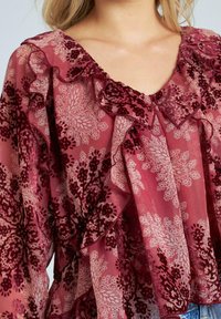 Blusa de color frambuesa con patrones florales en tonos más claros y más oscuros, con detalles de volantes en el escote y las mangas.