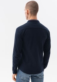 Musta pitkähihaisen paita, jossa on kauluskenttä, napitettu hihansuu ja sileä pinta, yhdistettynä vaaleansinisiin farkkuihin.