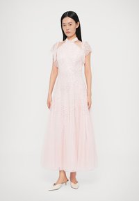 Hosszú rózsaszín ruha texturált flitterekkel, lebegő ujjakkal és magas nyakkivágással. A szoknya a padlóig ér, áttetsző, puha anyagból készült.