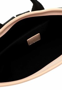 Interior negro de una bolsa con un forro suave de un rosa texturizado y un borde exterior liso. Se puede ver una pequeña etiqueta de cuero en tono beige con costuras.